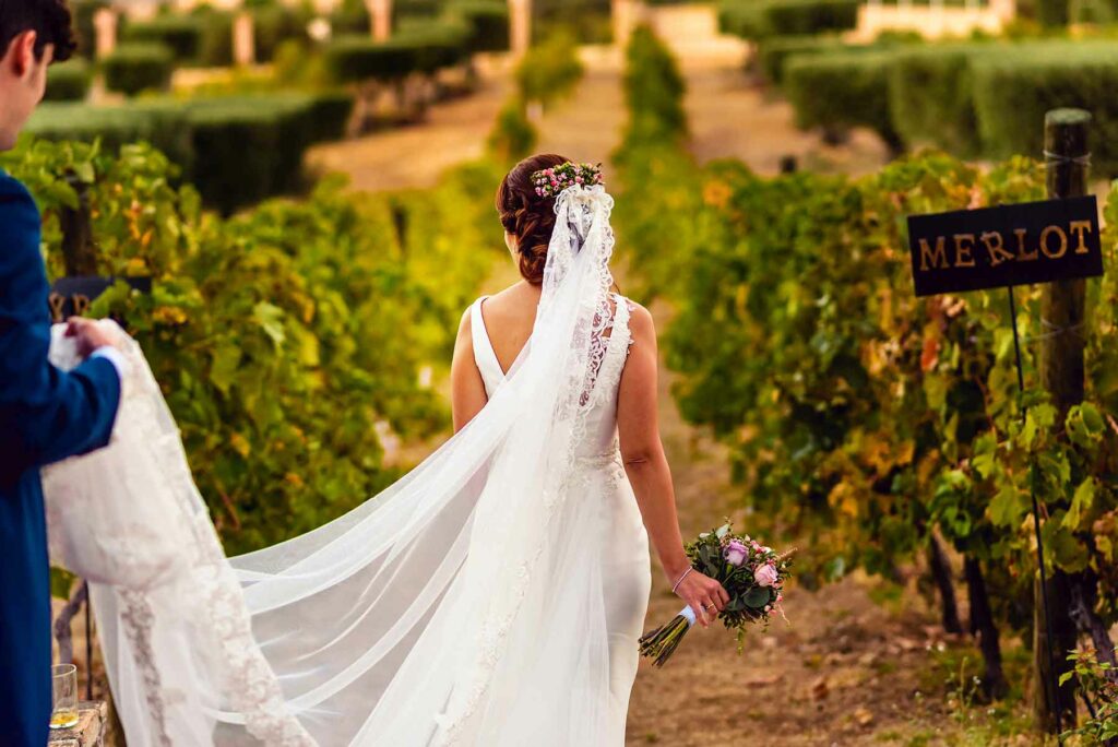 Person in a white wedding dress walking in a vineyard and carrying a bouquet