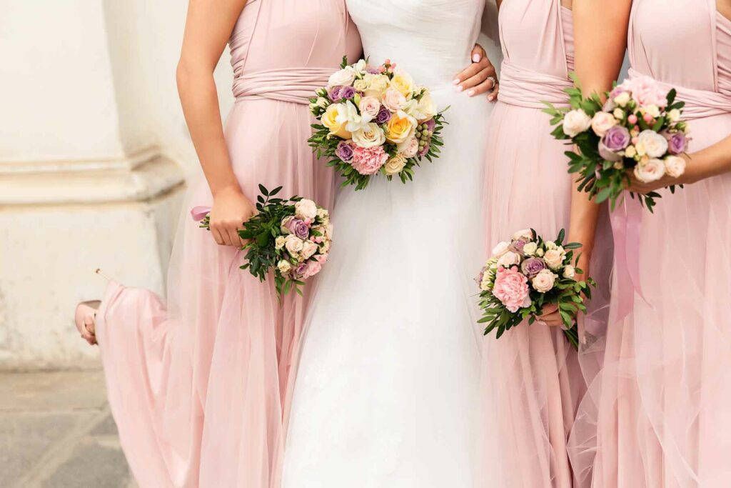 Three bridesmaids in pink tulle dresses with their arms wrapped around a bride's waist