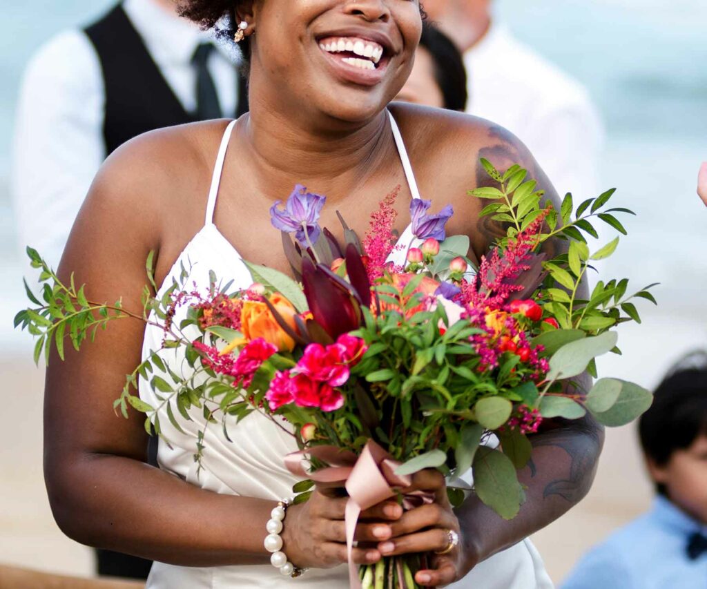 A bride smiling and holding a summer wedding bouquet of tropical flowers and greenery