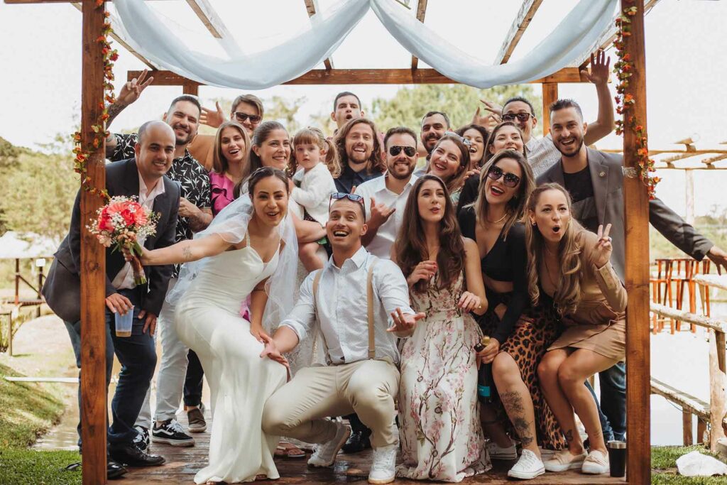 A couple surrounded by guests at their micro wedding under a wooden canopy posing for a group photo