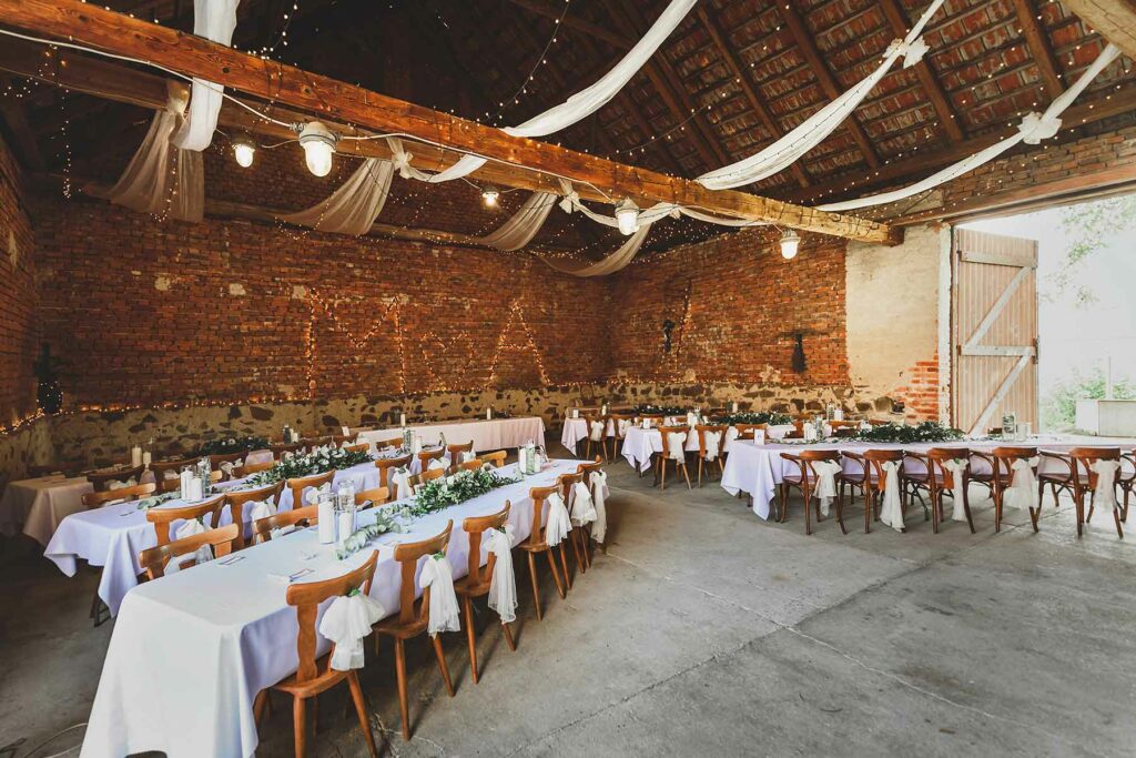 White fabric is draped from the ceiling. Twinkle lights contrast against exposed brick walls. White linens on reception tables are topped with greenery and candles. 