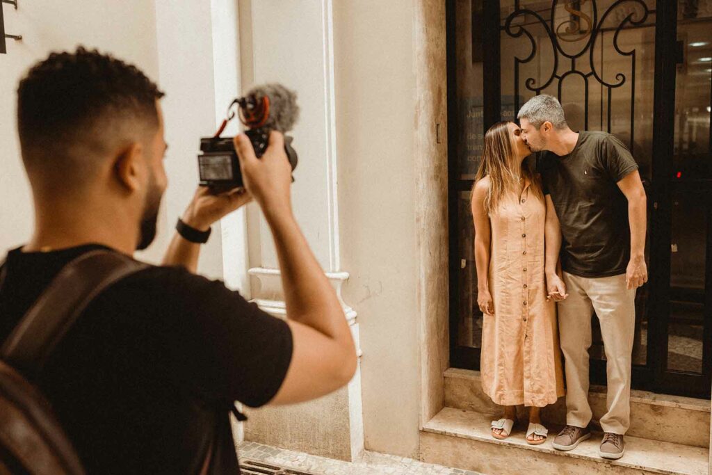 A couple kissing on the steps of a building as an engagement photographer takes their picture