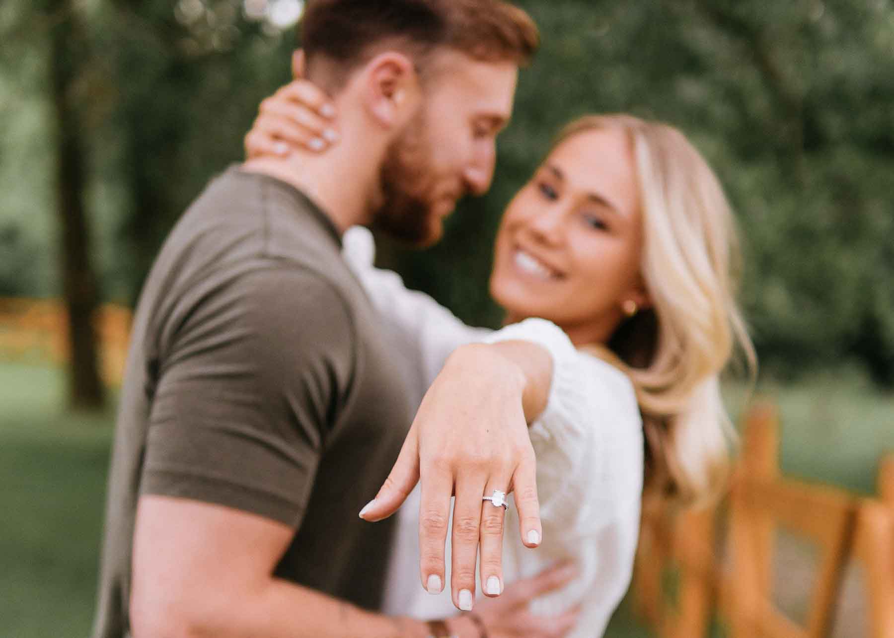 A couple embracing with a woman holding out her hand to show off an engagement ring