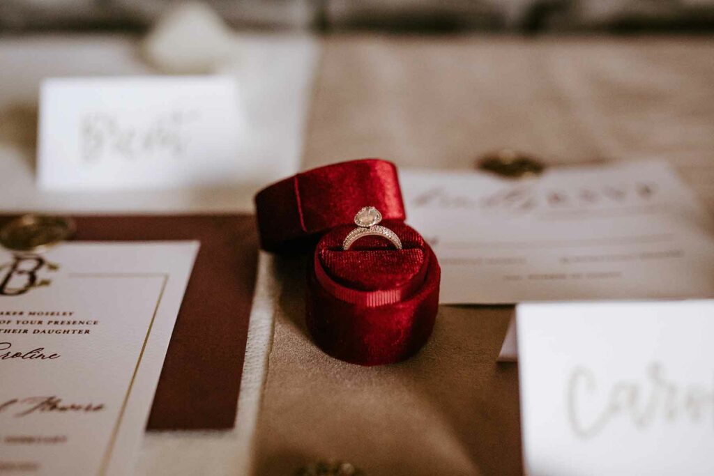 An engagement ring in a velvet box surrounded by wedding stationery