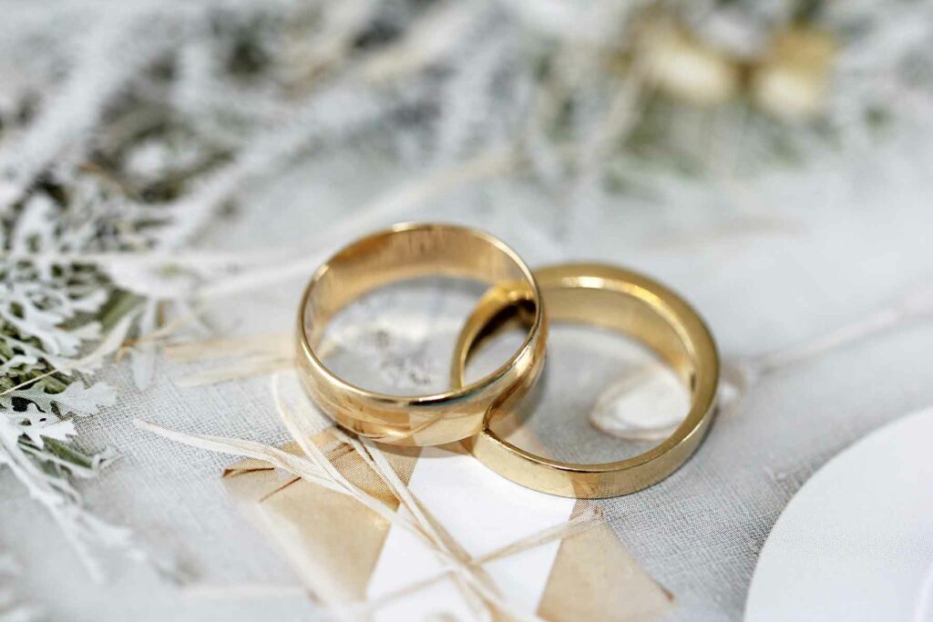 Two gold wedding bands on white textile with some frosty greenery in the top left corner