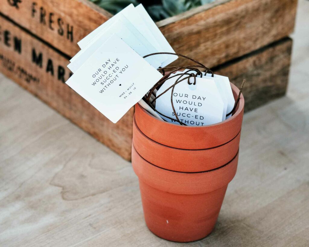 Wedding favor gift idea: Succulents in a wooden crate with terra cotta pots stacked and a tag that reads "our day would have succ-ed without you"