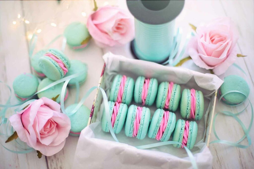 Wedding favor gift idea: Eight brightly colored macarons in a box surrounded by more macarons, ribbon and roses