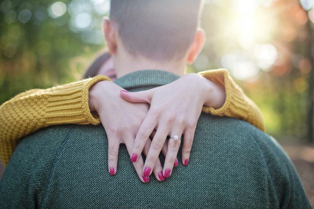 A woman's arms embracing a mans' neck showing off her engagement ring