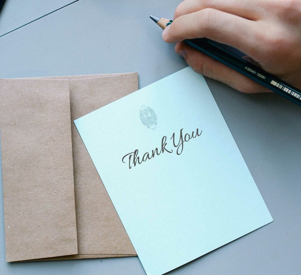 A hand holding a pencil about to write in a thank you card
