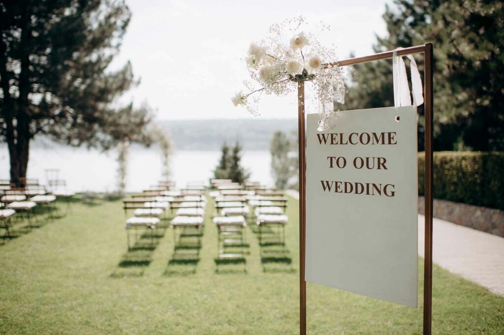 A sign that reads "welcome to our wedding" in front of a set of wedding guest chairs overlooking the ocean