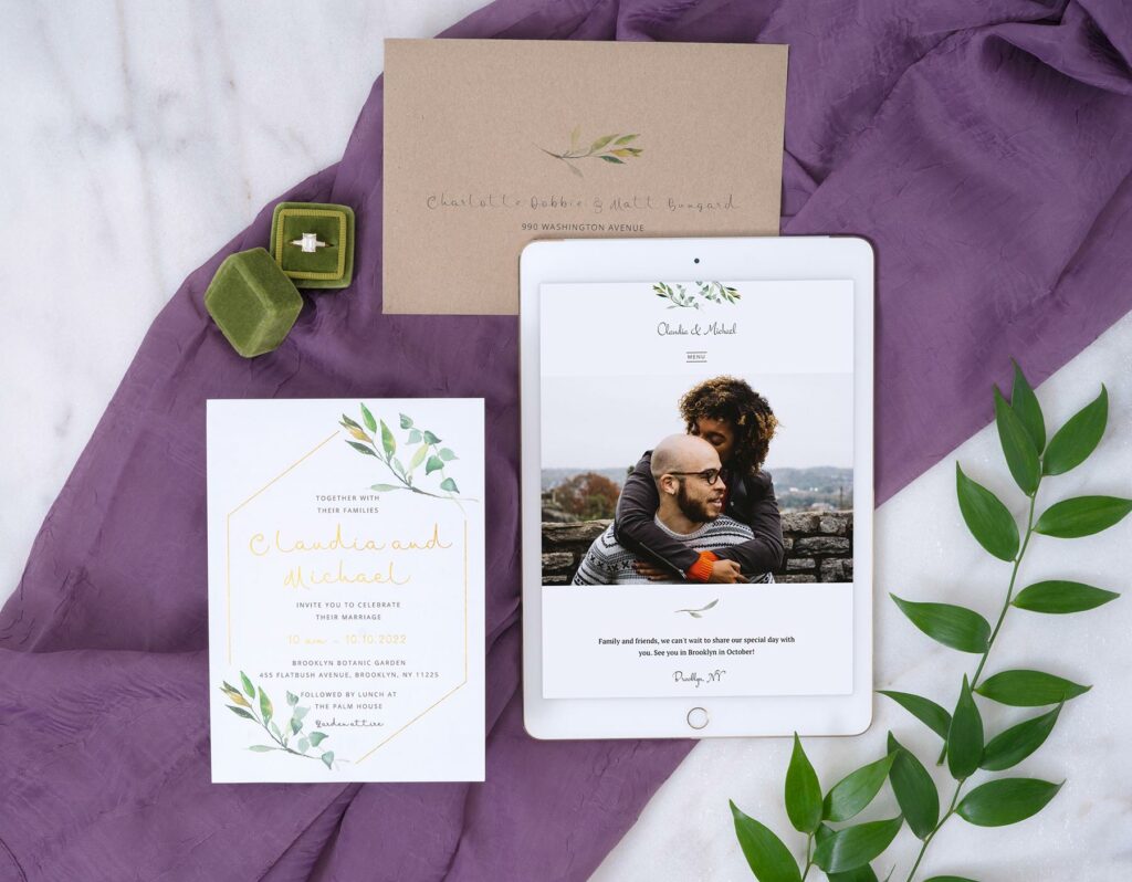 Joy's Garden Wedding invitation on a piece of cloth surrounded by a wedding ring in a velvet box, a matching envelope, and matching wedding website on a tablet featuring aa couple embracing