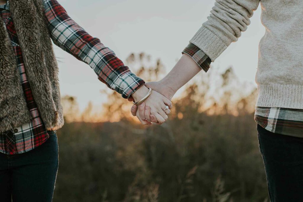 What to Wear in Engagement Photos: A woman wearing flannel and a faux fur vest holding hands with another woman wearing a sweater layered over flannel 