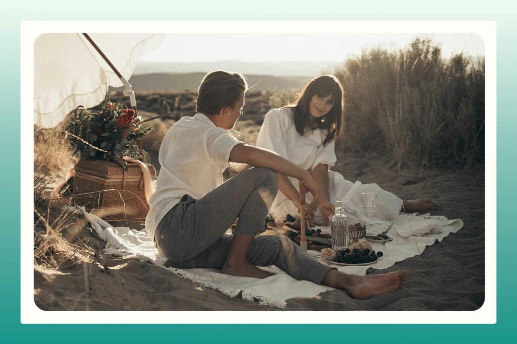 A couple preparing for a beach proposal with a picnic