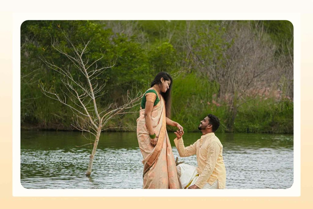A man on one knee proposing to a woman in front of a body of water and greenery