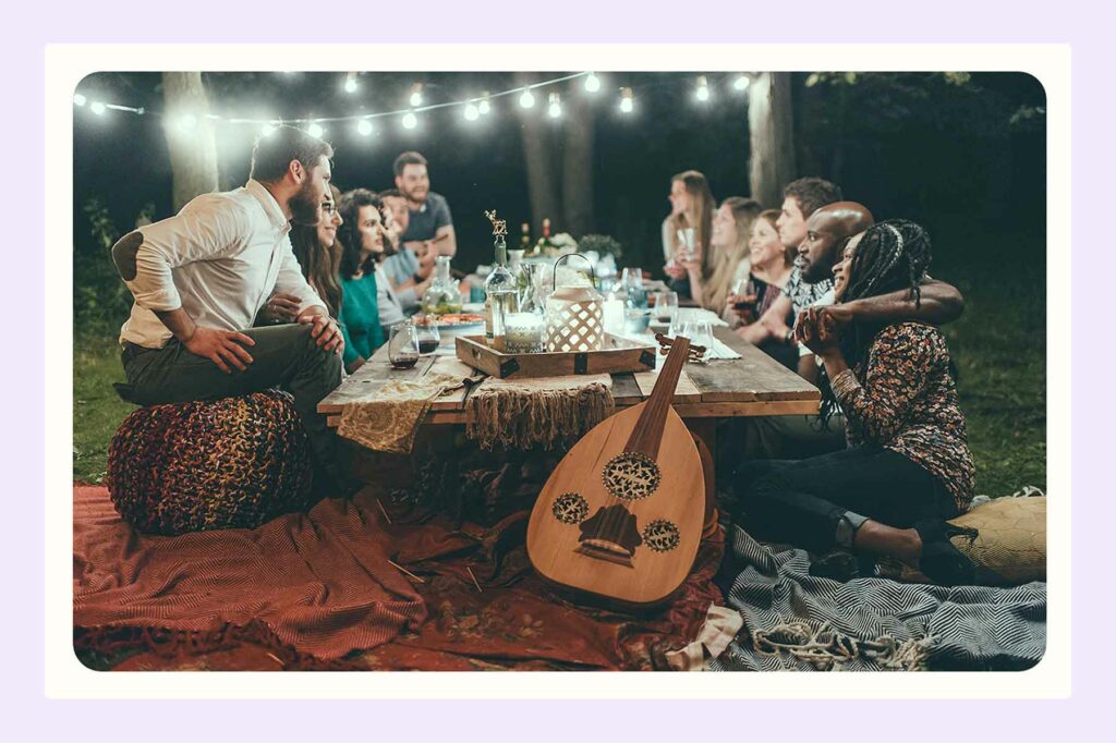 A gathering of family and friends around a rustic wood table with a guitar leaning on blankets