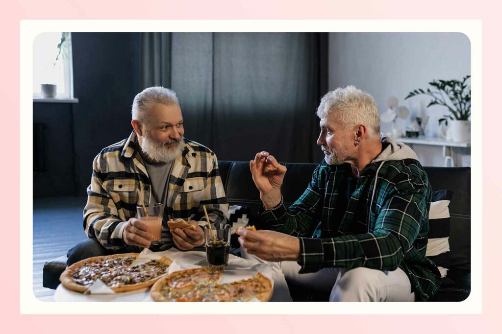 Two men sitting in a living room enjoying a meal of pizza together