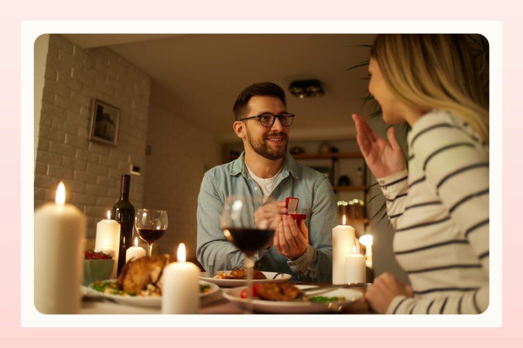 Man holding ring box out to surprised woman during a candlelit dinner at home