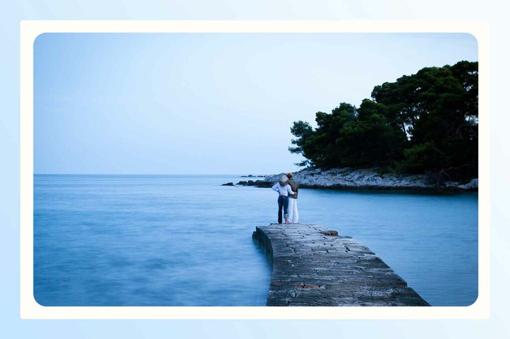 A couple embracing at the end of a pier looking out at a water before their beach proposal