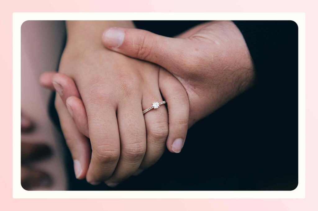Two people holding hands with a simple engagement ring in focus