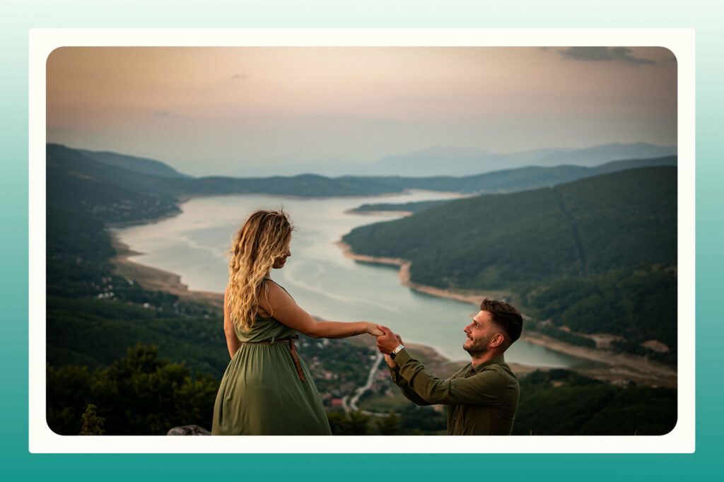 A man proposing on top of a cliff overlooking a body of water at sunset