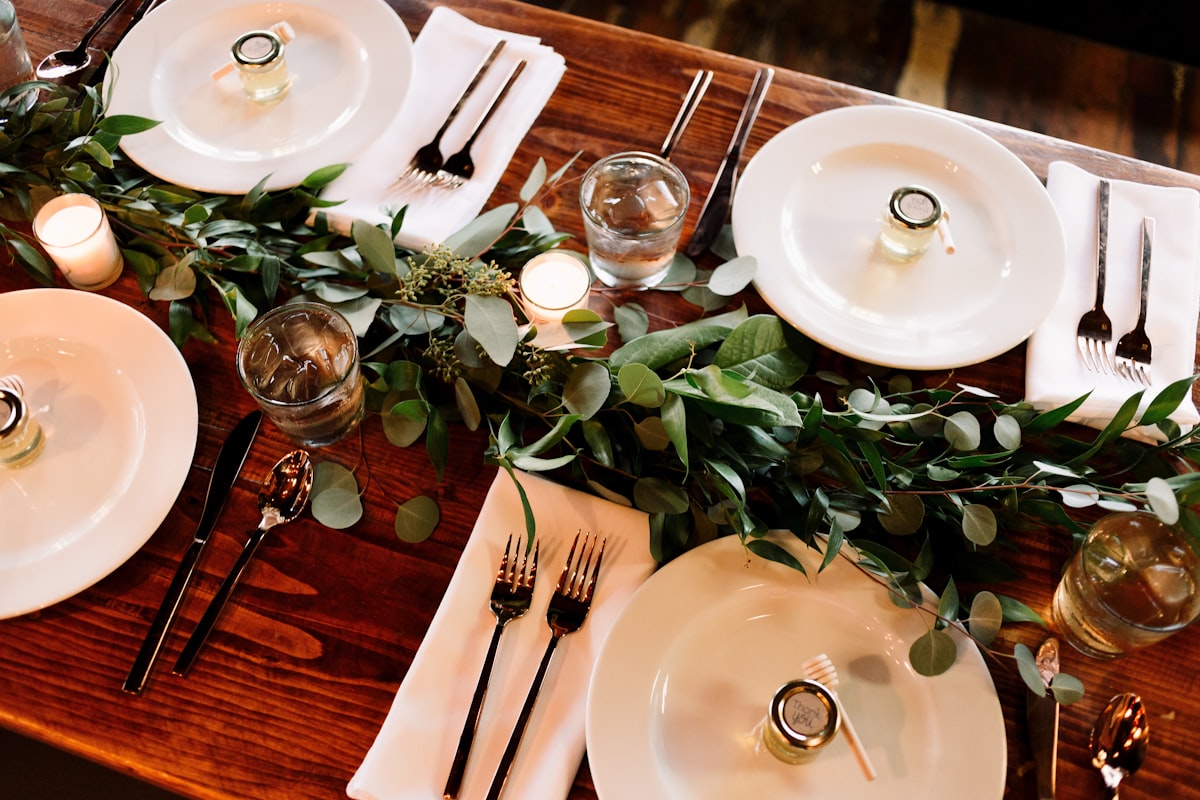 Outdoor wedding reception table set with floral centerpieces, glassware, and linen napkins under soft evening light