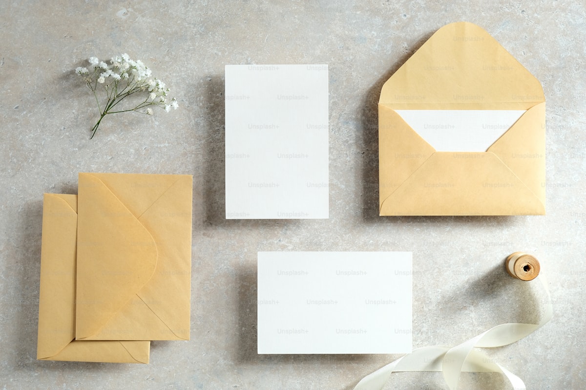 Kraft paper wedding invitations styled flat lay with ribbon and flowers