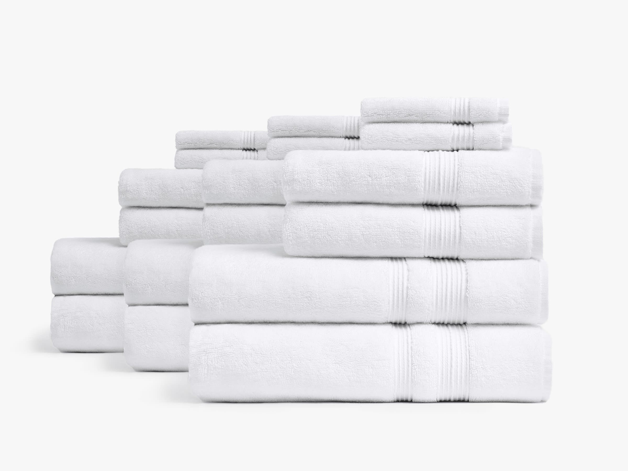White bath towel set folded and stacked with bath towels, hand towels and washclothes on a white background